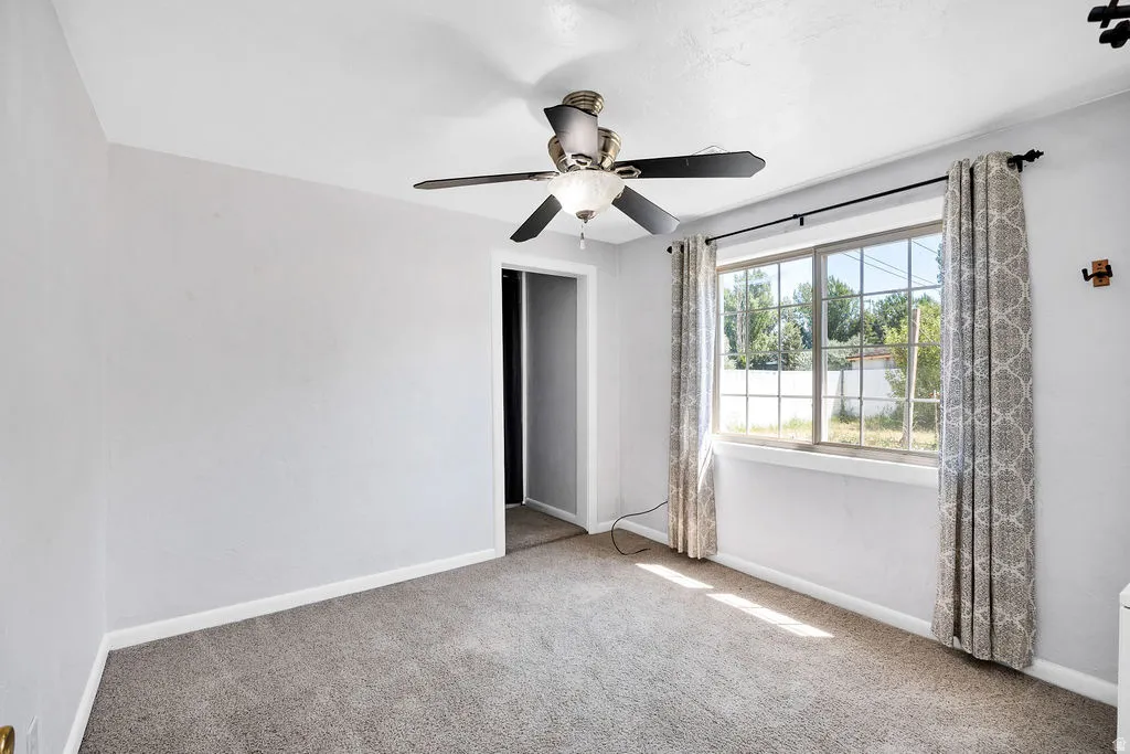 Carpeted room featuring a large window with white muntins, light gray walls, white baseboards, and a ceiling fan with integrated lighting