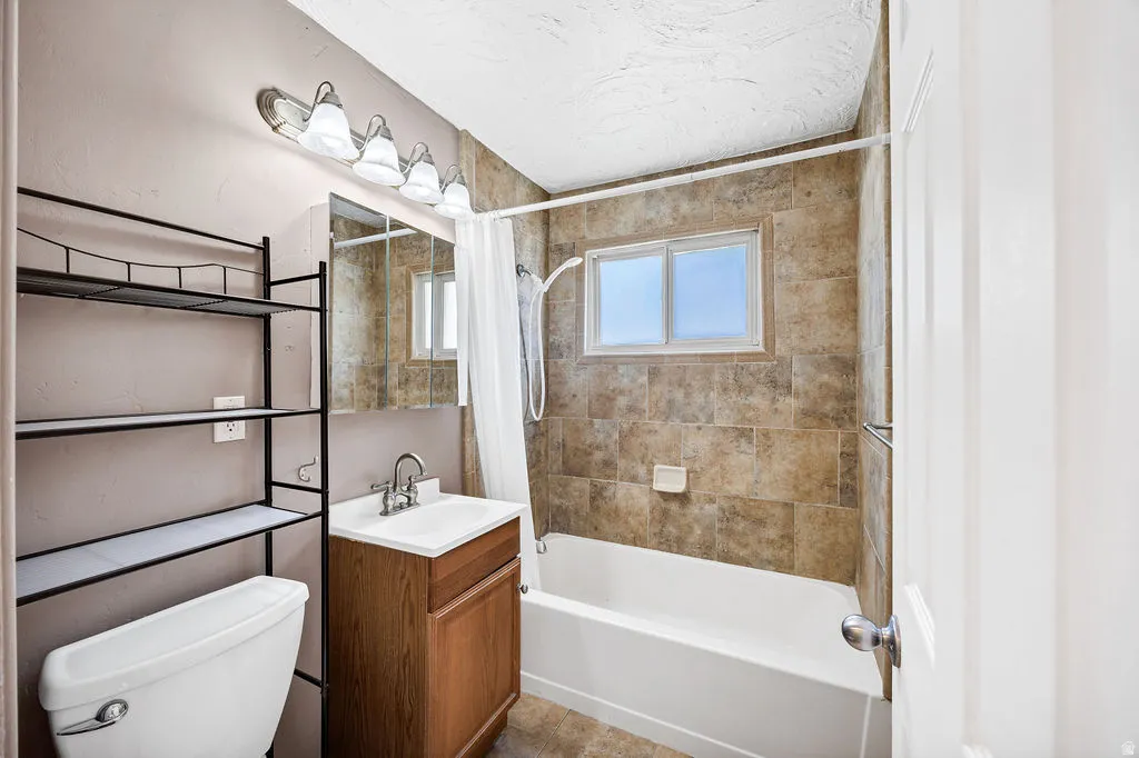 Bathroom featuring a tiled shower surround, integrated window, wood-finish vanity with a white basin, and a mirrored medicine cabinet