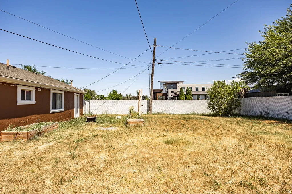 Expansive backyard featuring a brown exterior building, white trim windows, and raised garden beds