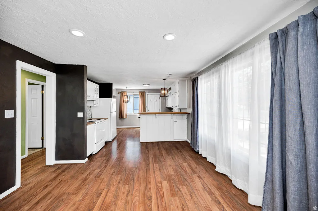 Open-concept living area featuring wood-finish flooring, recessed lighting, and a kitchen with white cabinetry and a light wood-finish countertop