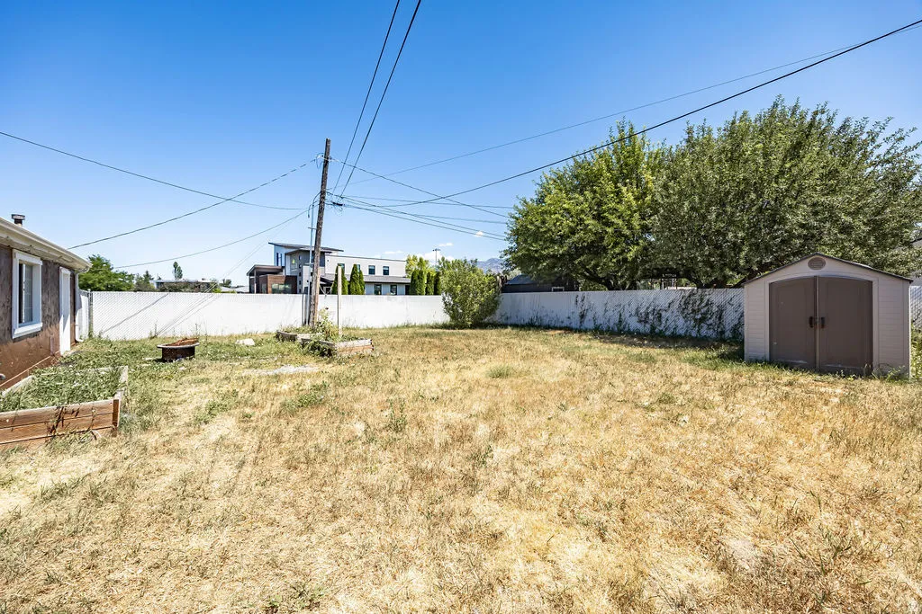 Expansive backyard featuring a storage shed, white privacy fencing, and mature trees