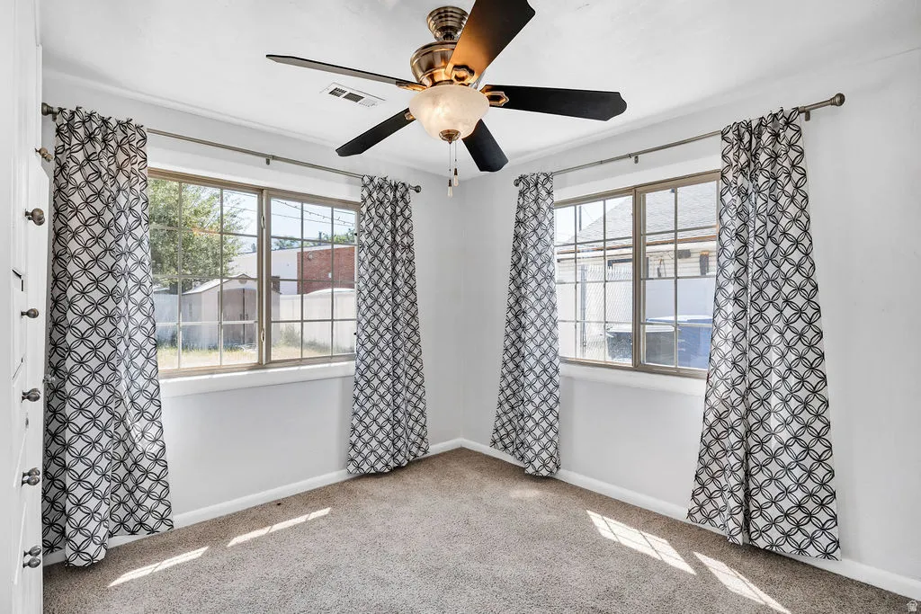 Carpeted room featuring a ceiling fan with integrated lighting, two windows with gridded panes, and white painted walls