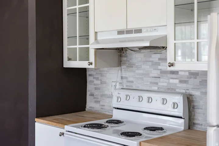 Kitchen featuring a white electric range, light wood-finish countertops, and a gray-toned subway tile backsplash