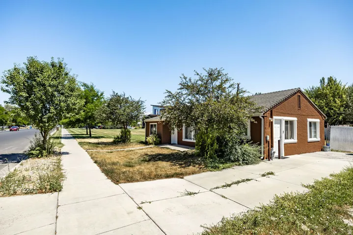 Brown exterior with white trim, featuring a side driveway, concrete sidewalk, and mature landscaping