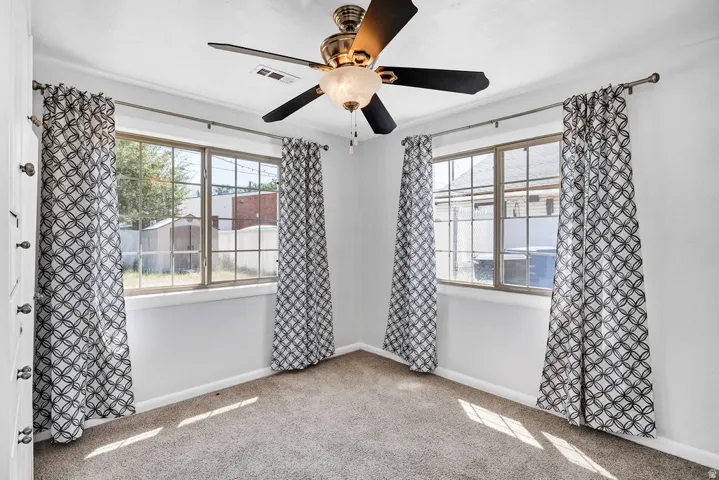 Carpeted room featuring a ceiling fan with integrated lighting, two windows with gridded panes, and white painted walls