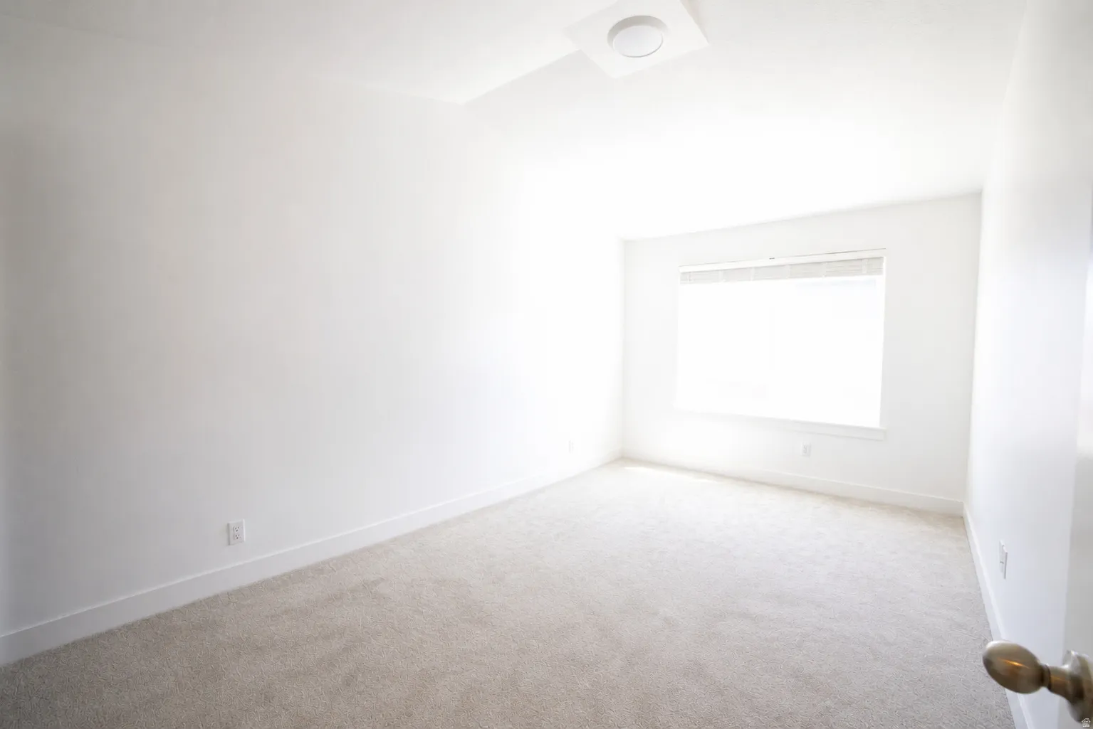 Bright room with light-colored carpet flooring, white walls, and a large window with blinds