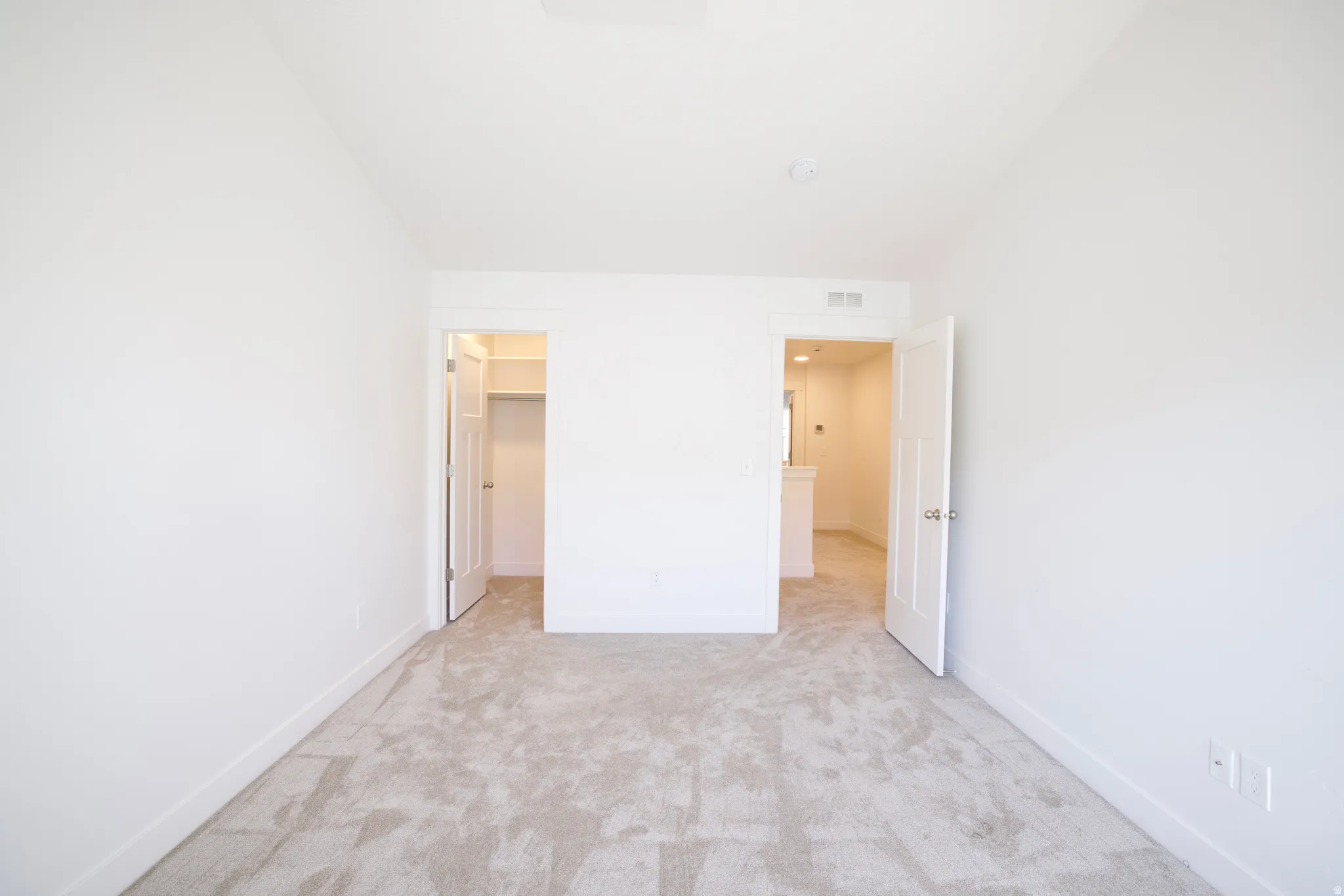 Light-filled room featuring neutral-toned carpeting, crisp white walls, white trim, and two doorways