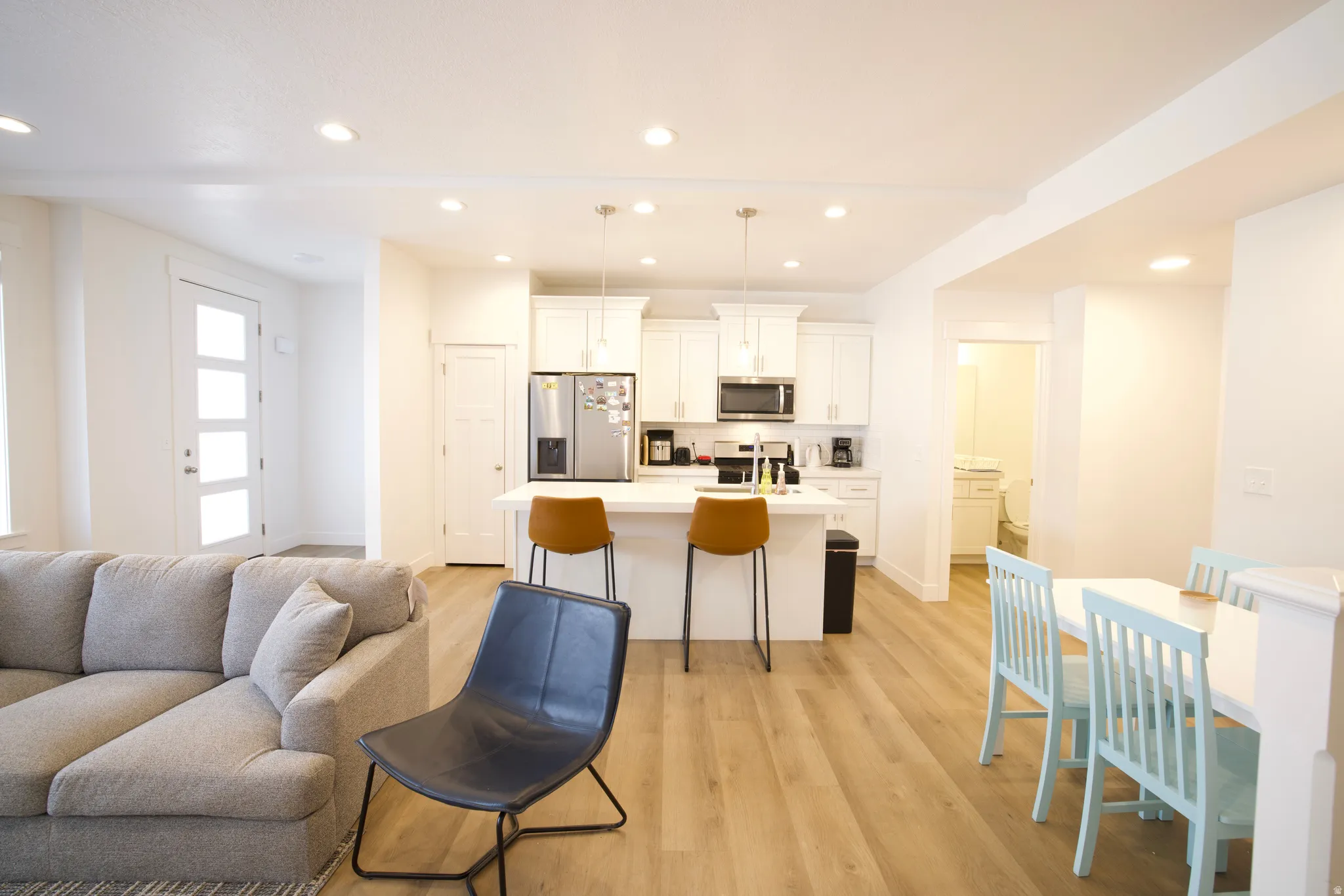 Open-concept living area with wood-finish flooring, recessed lighting, and a white kitchen featuring a center island with pendant lighting and stainless steel appliances
