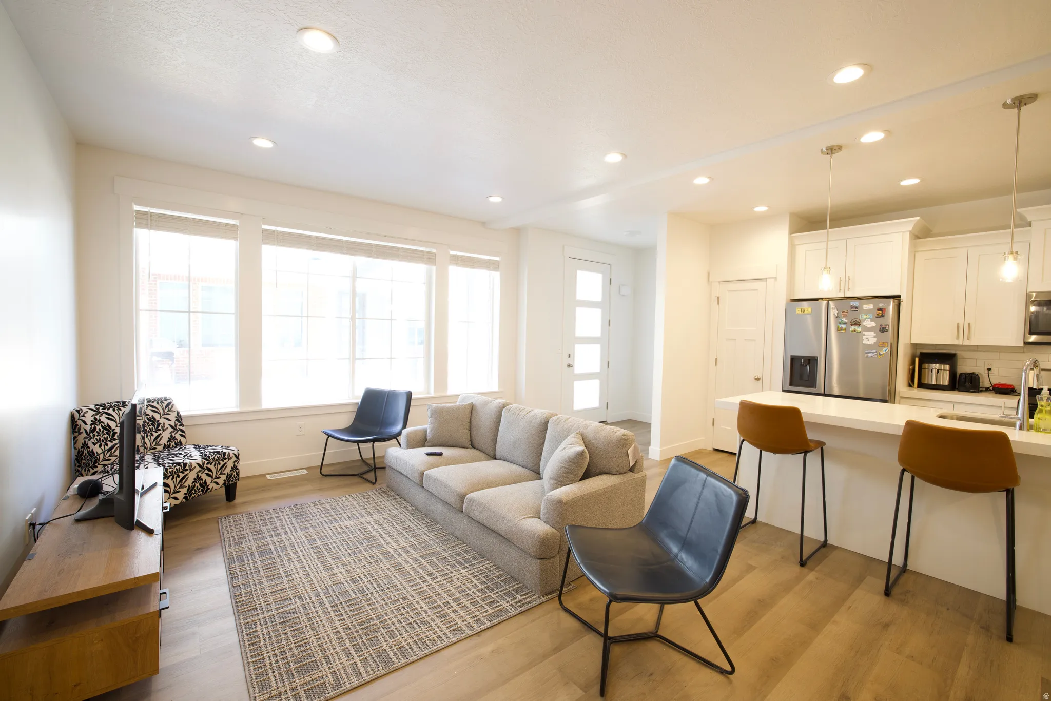 Open-concept living area featuring a kitchen island with seating, stainless steel appliances, recessed lighting, and wood-finish flooring