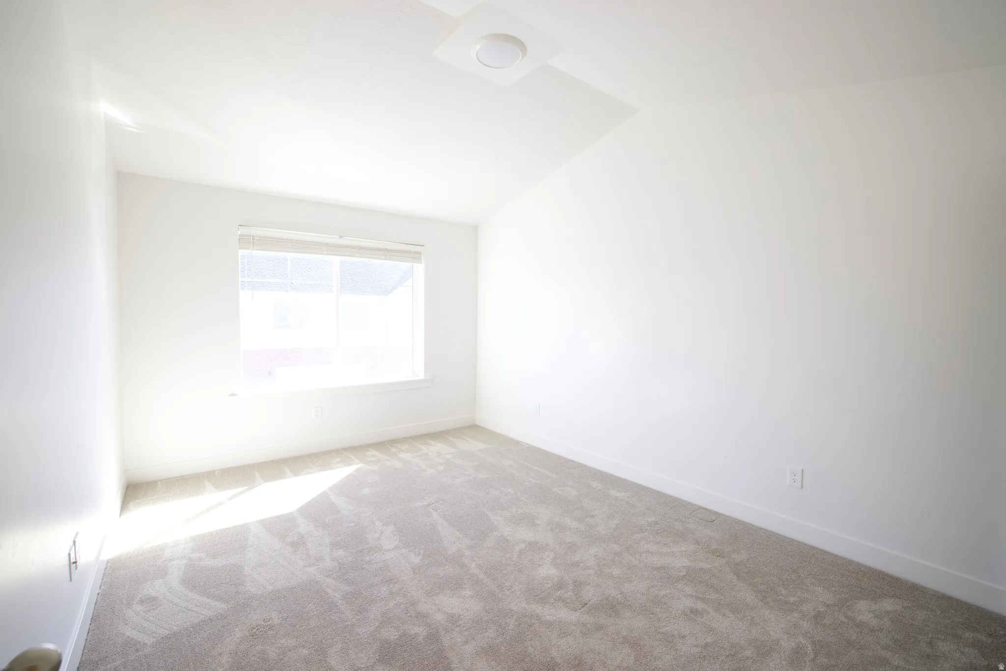 Bright room featuring a window with blinds, neutral-toned carpet, white walls, and a ceiling-mounted light fixture