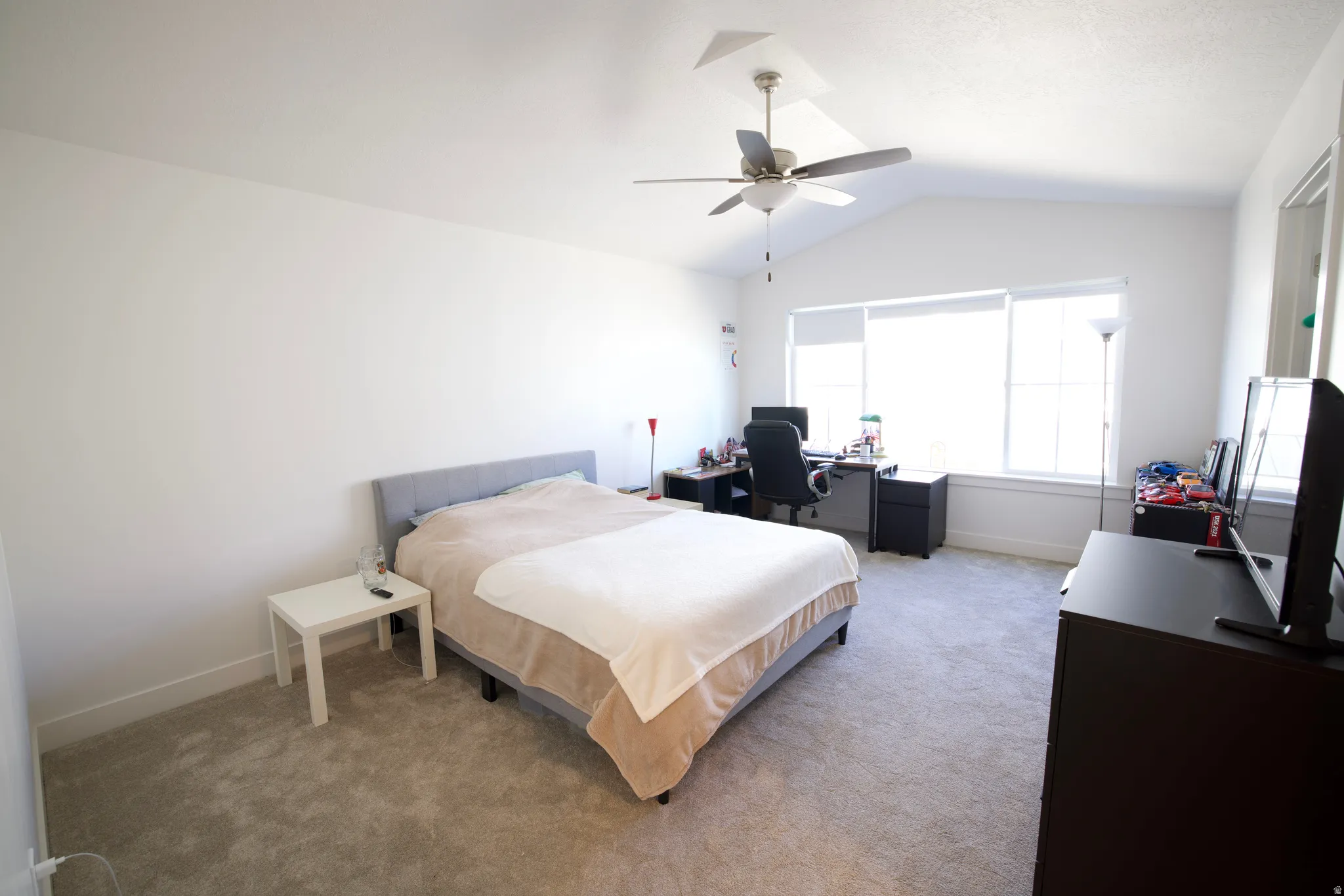 Spacious room featuring vaulted ceilings, a ceiling fan, broad window, and carpet flooring