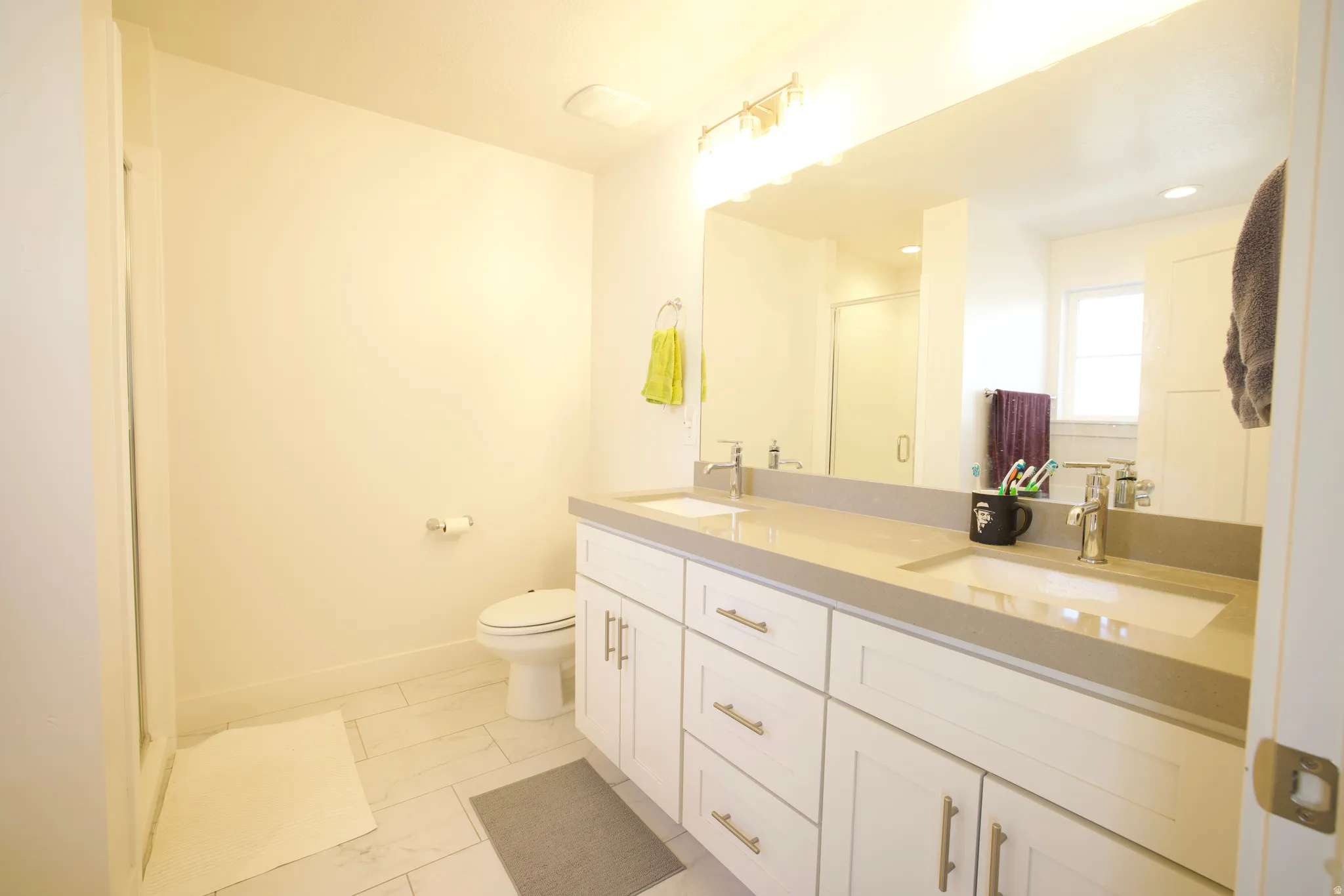 Double vanity with integrated sinks, light-toned countertop, and white cabinetry featuring brushed nickel hardware