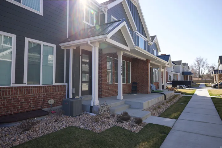 Contemporary townhome exterior featuring gray siding, red brick accents, a covered front porch, and a dark entry door with frosted glass panels