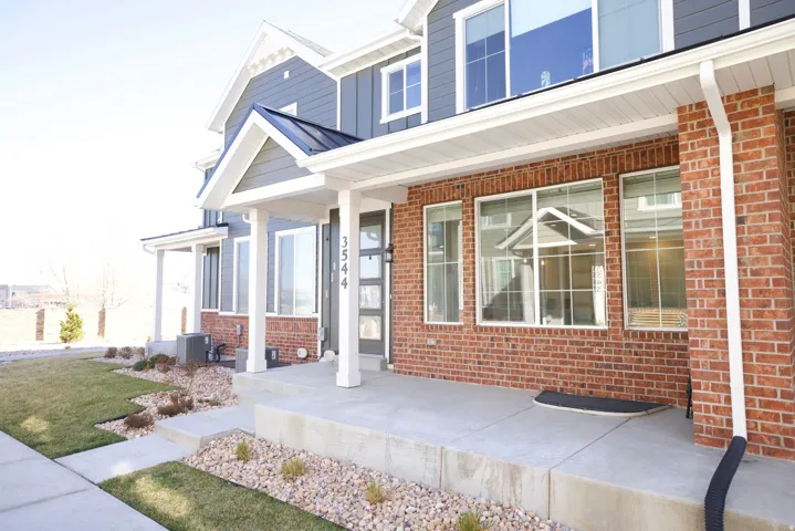Exterior showcasing a modern two-story design with brick and siding facade, an inviting covered entry, a concrete walkway, and landscaped rock beds with plantings