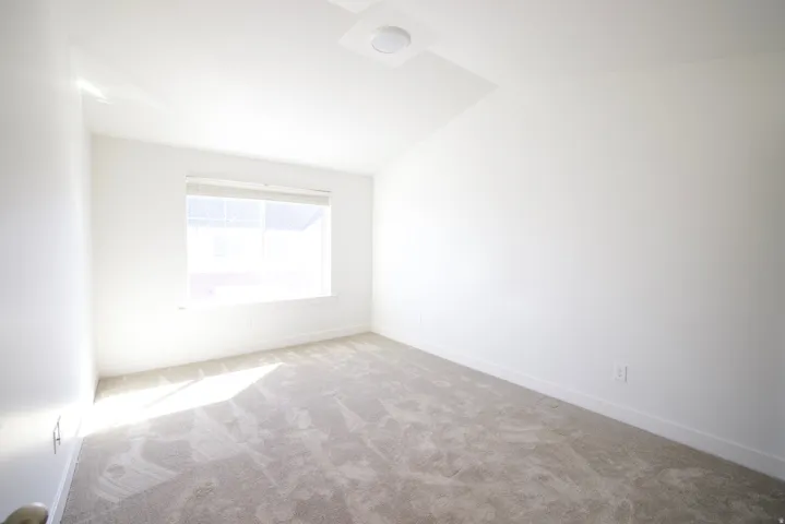 Bright room featuring a window with blinds, neutral-toned carpet, white walls, and a ceiling-mounted light fixture