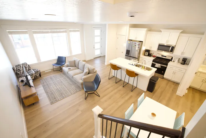 Open-concept living space featuring wood-finish flooring, a white kitchen with stainless steel appliances, a kitchen island with seating, a dining area, and large windows