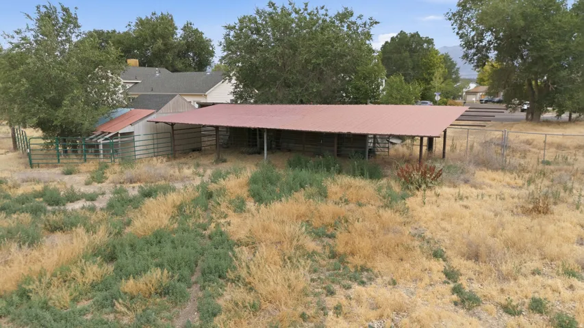 Expansive property featuring a large open-sided barn with a red metal roof, a smaller enclosed shed, and a fenced area