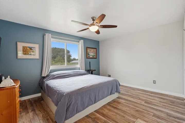 Spacious bedroom featuring wood-finish flooring, a ceiling fan with integrated lighting, and a window with white trim