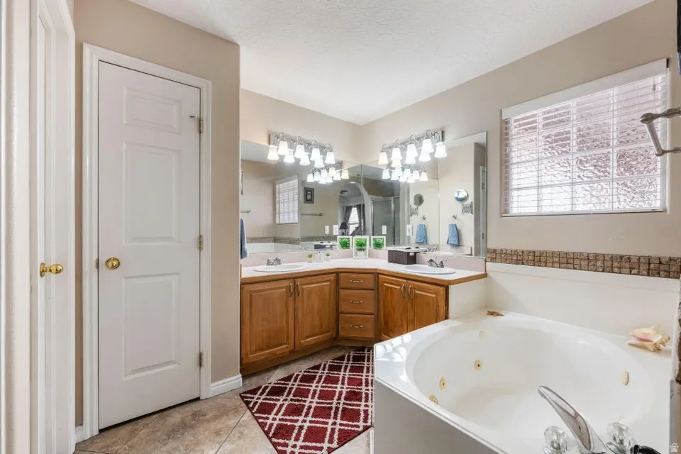 Bathroom featuring a corner jetted tub, dual vanity with wood-finish cabinetry, and tiled flooring