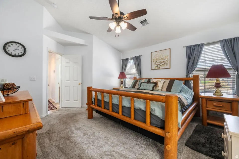 Carpeted bedroom with vaulted ceilings, two windows with blinds, a ceiling fan, and a solid core door