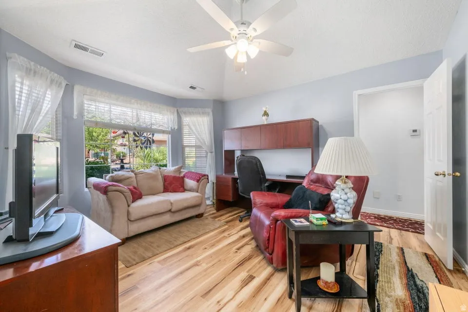 Light-filled room featuring wood-finish flooring, a bay window with blinds, and a ceiling fan