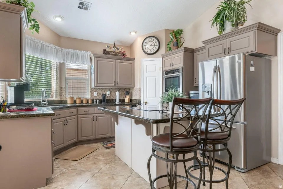 Kitchen featuring an island with seating, stainless steel appliances, recessed lighting, tile flooring, and a window with blinds