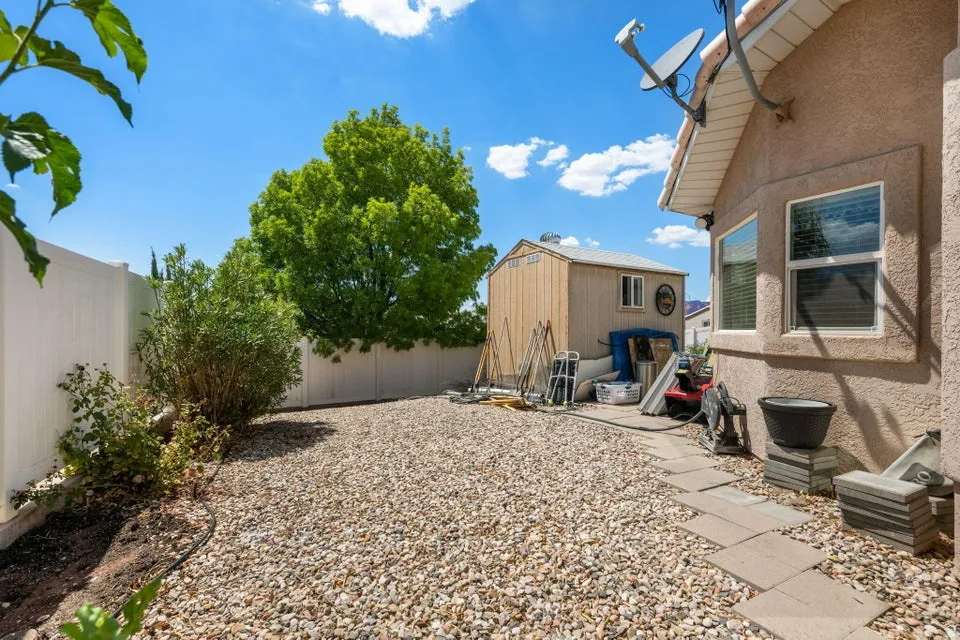 Gravel patio area featuring a detached storage shed, stucco exterior, and white vinyl fencing