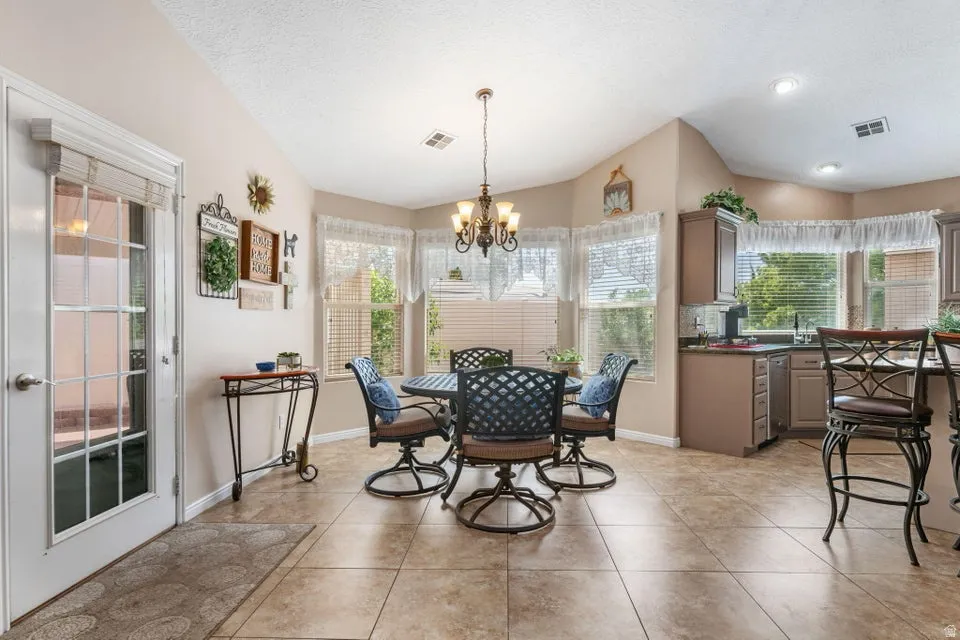 Kitchen dining area featuring neutral tile flooring, a bay window with blinds, a multi-light chandelier, a glass-paned door, and recessed lighting