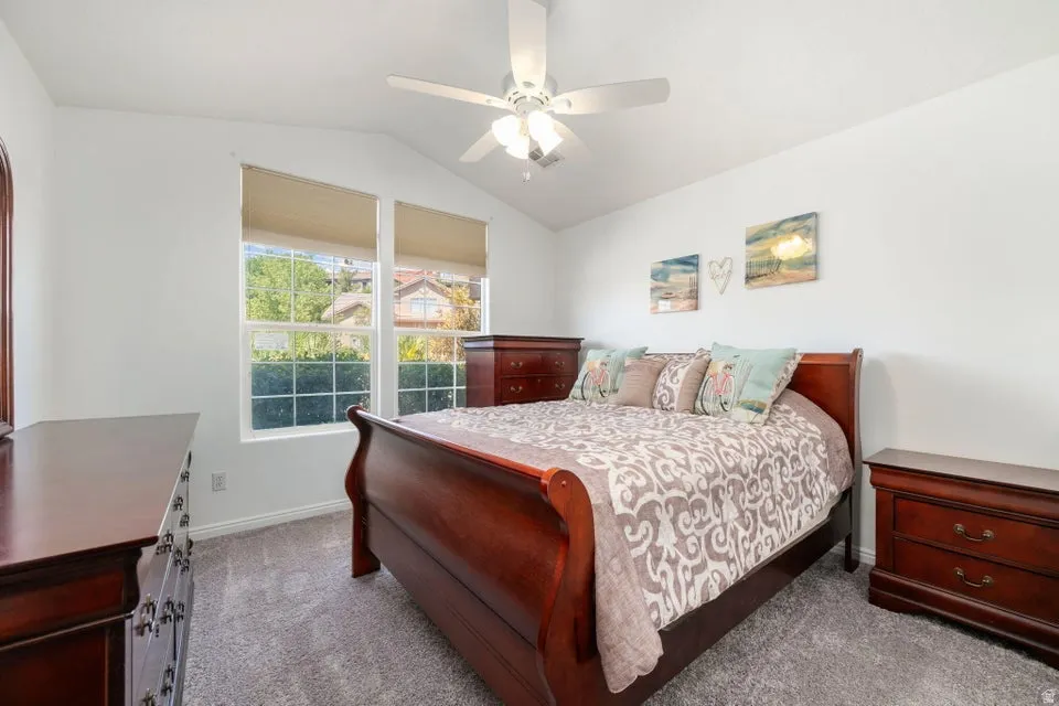 Vaulted ceiling bedroom with a ceiling fan light fixture and two windows featuring blinds