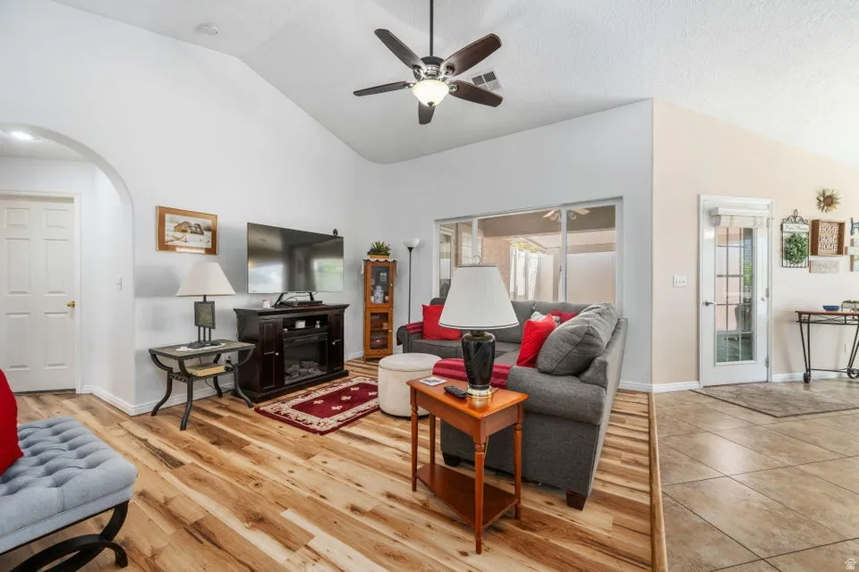 Vaulted ceilings enhance this living area featuring wood-finish flooring, a ceiling fan, and large windows