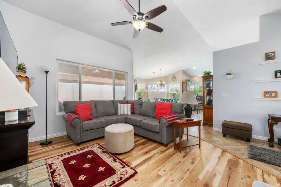 Spacious living area featuring vaulted ceilings, a ceiling fan with integrated lighting, and wood-finish flooring