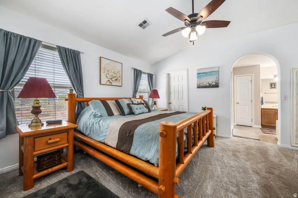 Spacious room featuring vaulted ceilings, a ceiling fan with integrated lighting, two windows with blinds, and neutral carpet flooring