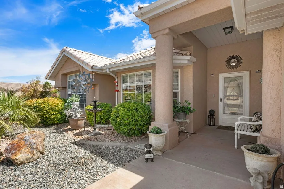 Inviting front entry featuring stucco exterior, a columned porch, a tiled roof, and xeriscaped landscaping with mature shrubs and rock ground cover