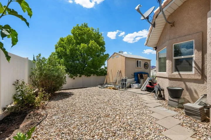 Gravel patio area featuring a detached storage shed, stucco exterior, and white vinyl fencing