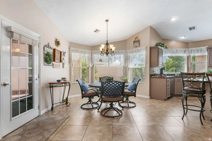 Kitchen dining area featuring neutral tile flooring, a bay window with blinds, a multi-light chandelier, a glass-paned door, and recessed lighting