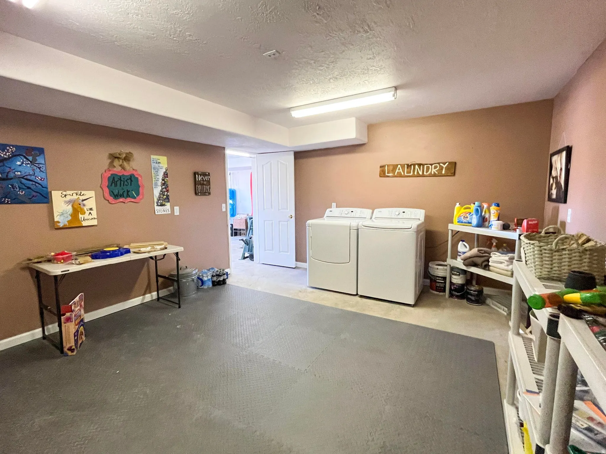Dedicated laundry space featuring a white washer and dryer pair, an adjacent shelving unit for storage, and a light-colored door providing access to an additional room