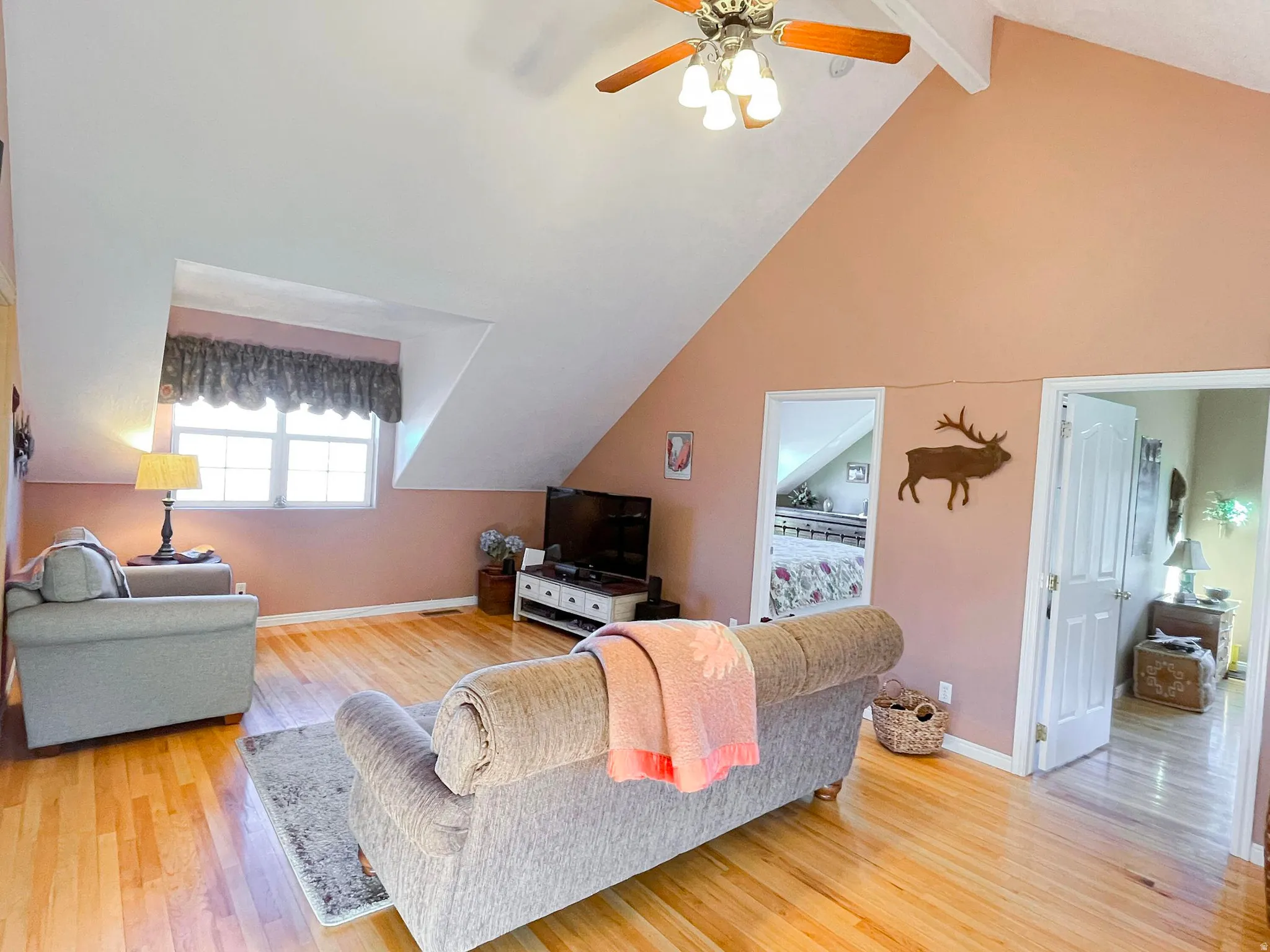 Spacious room with a vaulted ceiling, wood-finish flooring, ceiling fan, and multiple windows