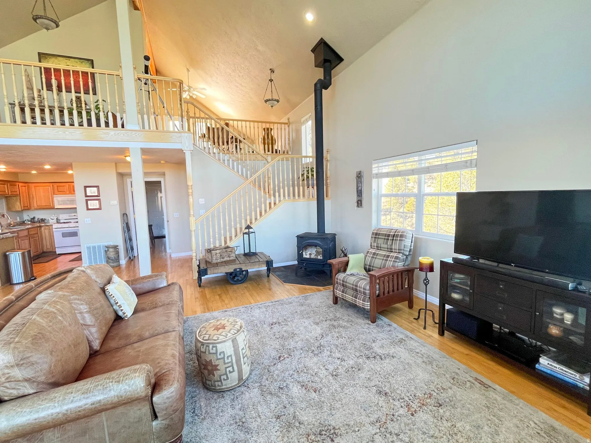 Vaulted ceiling great room featuring a wood-burning stove with a tall black flue, hardwood-finish flooring, and a multi-level staircase with wood railings