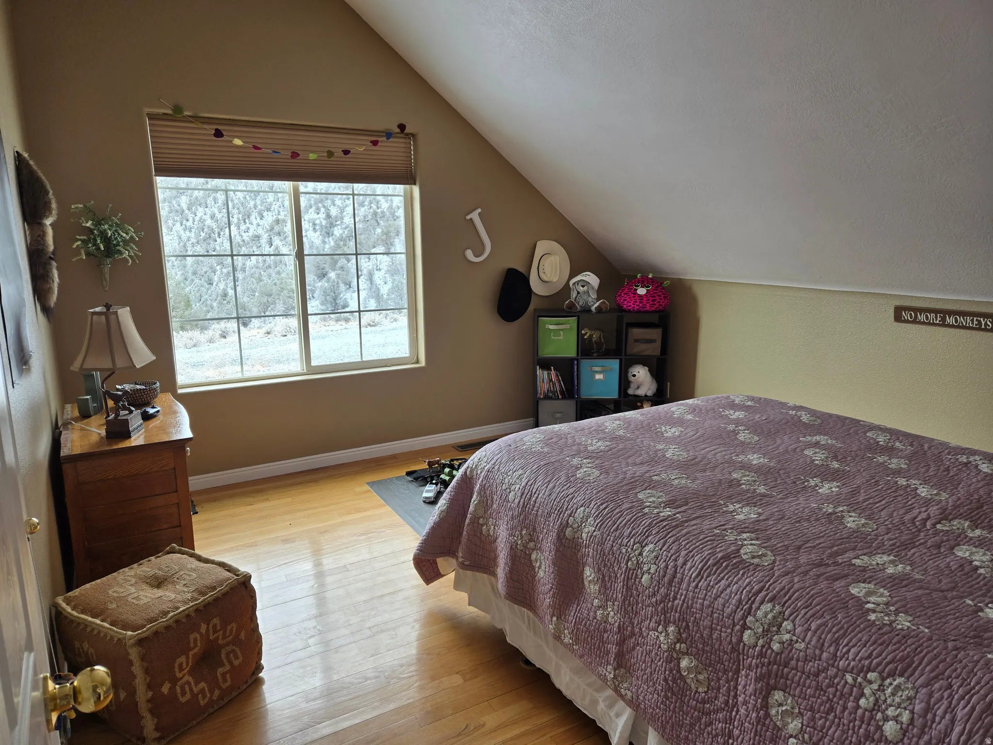 Bedroom featuring a window with a cellular shade, hard-surface flooring, and a sloped ceiling