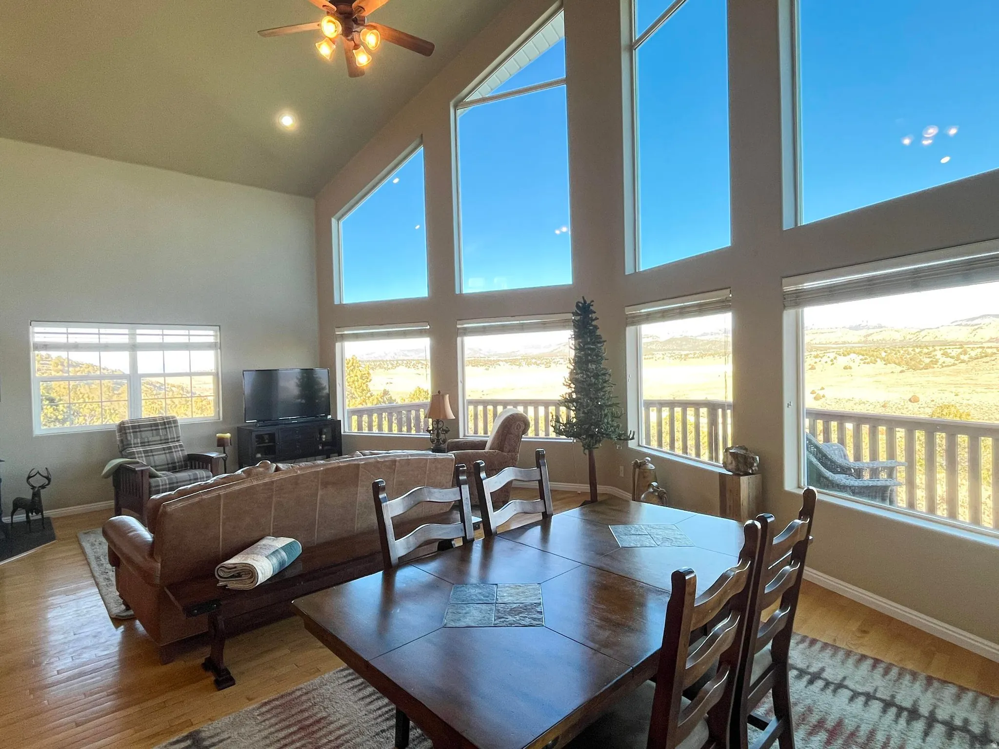 Spacious living area featuring large windows, vaulted ceilings, a ceiling fan, wood-finish flooring, and a fireplace with a dark mantel