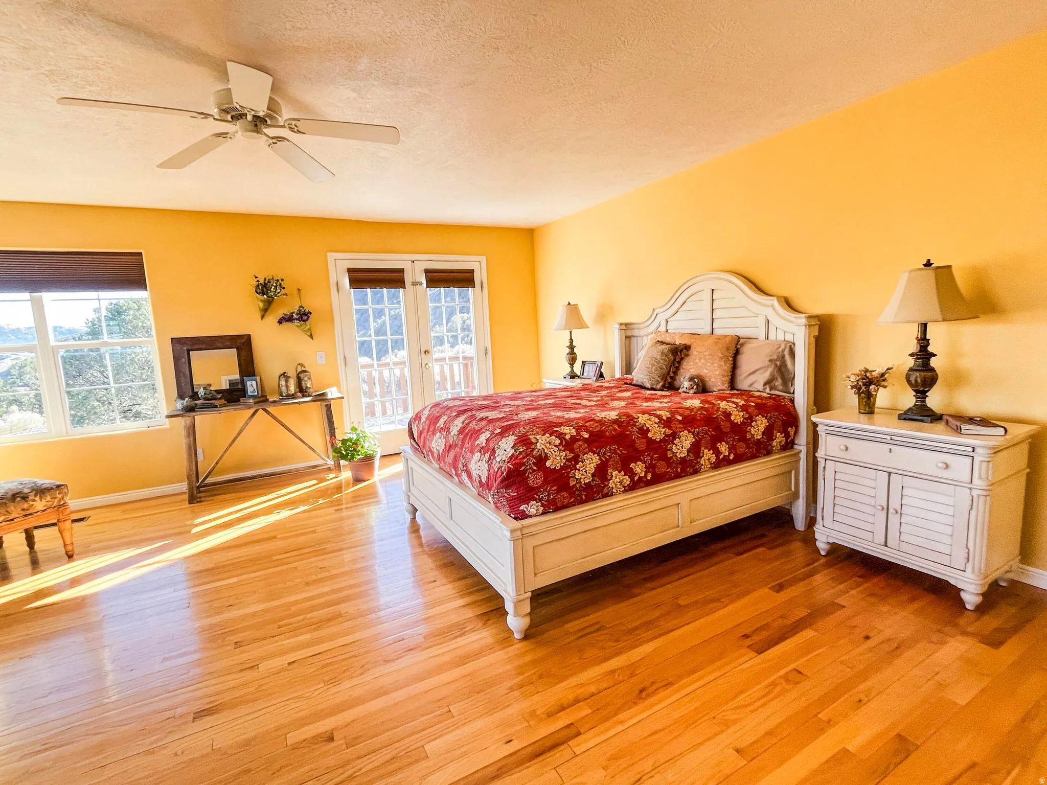Hardwood flooring throughout featuring a ceiling fan, dual windows with blinds, and French doors