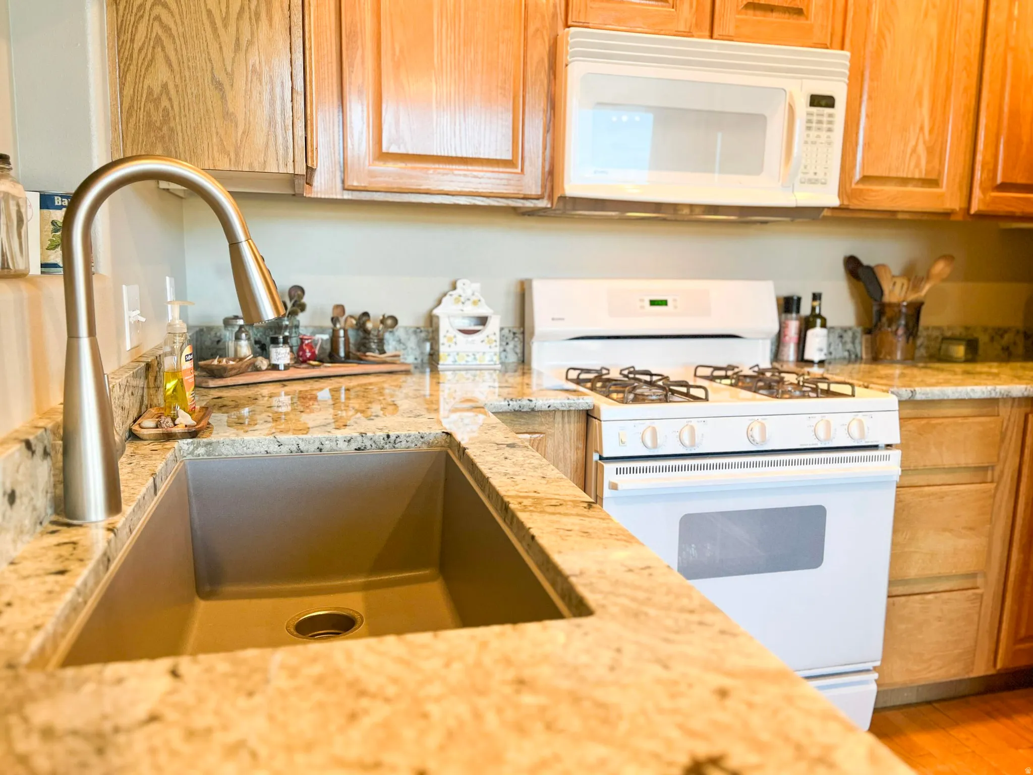 Kitchen featuring granite countertops, wood cabinetry, a gooseneck faucet, an undermount sink, and a white range with an oven
