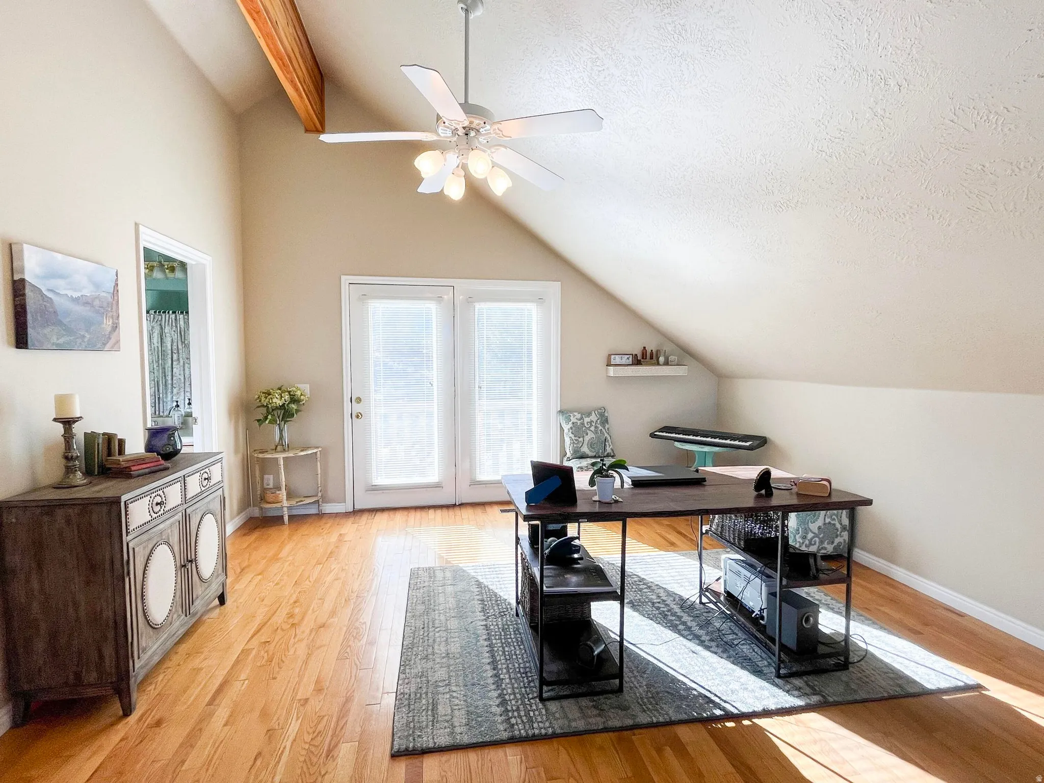 Bright room featuring wood-finish flooring, vaulted ceiling with exposed beam, and a ceiling fan