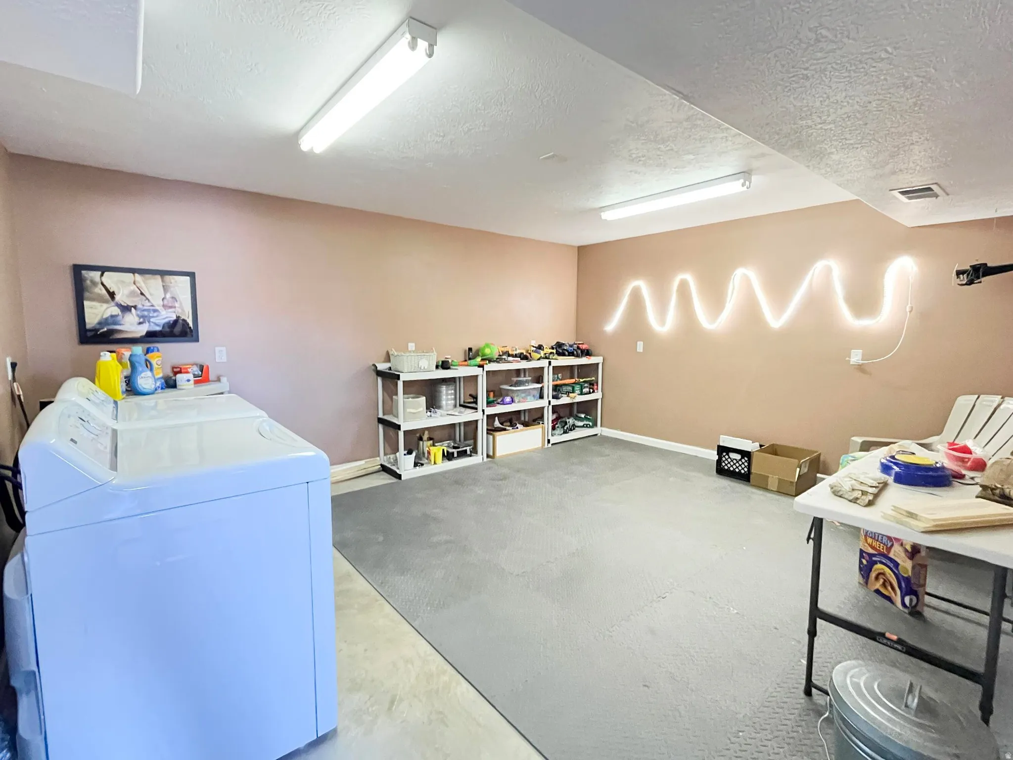 Spacious utility area featuring a concrete floor with partial rubber matting, fluorescent ceiling lights, and painted walls