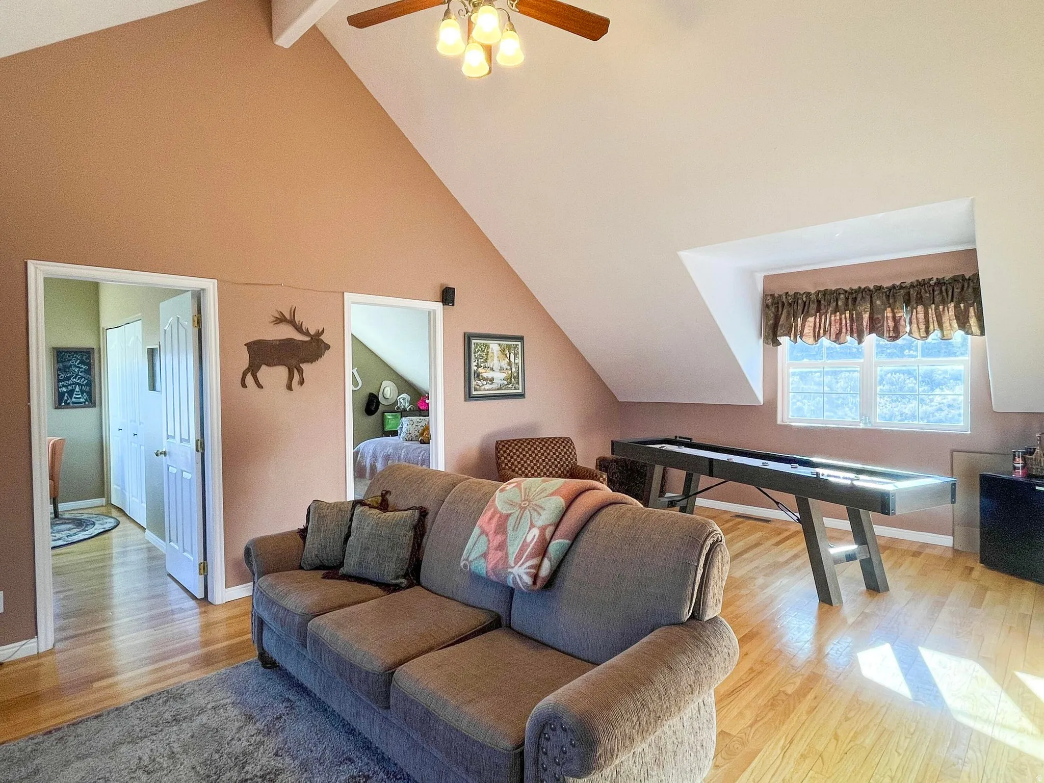 Vaulted ceilings with exposed beams and a ceiling fan enhance this space featuring wood-finish flooring