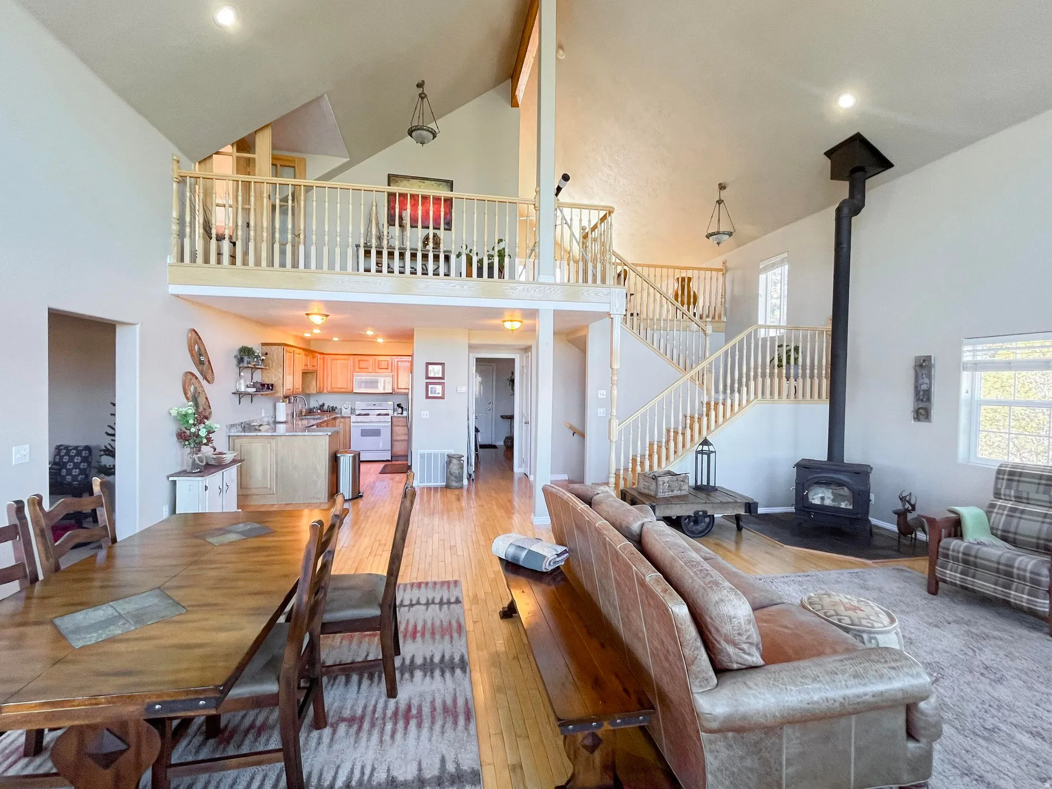 Vaulted ceilings enhance this open-concept living space, featuring hardwood flooring and a prominent wood-burning stove