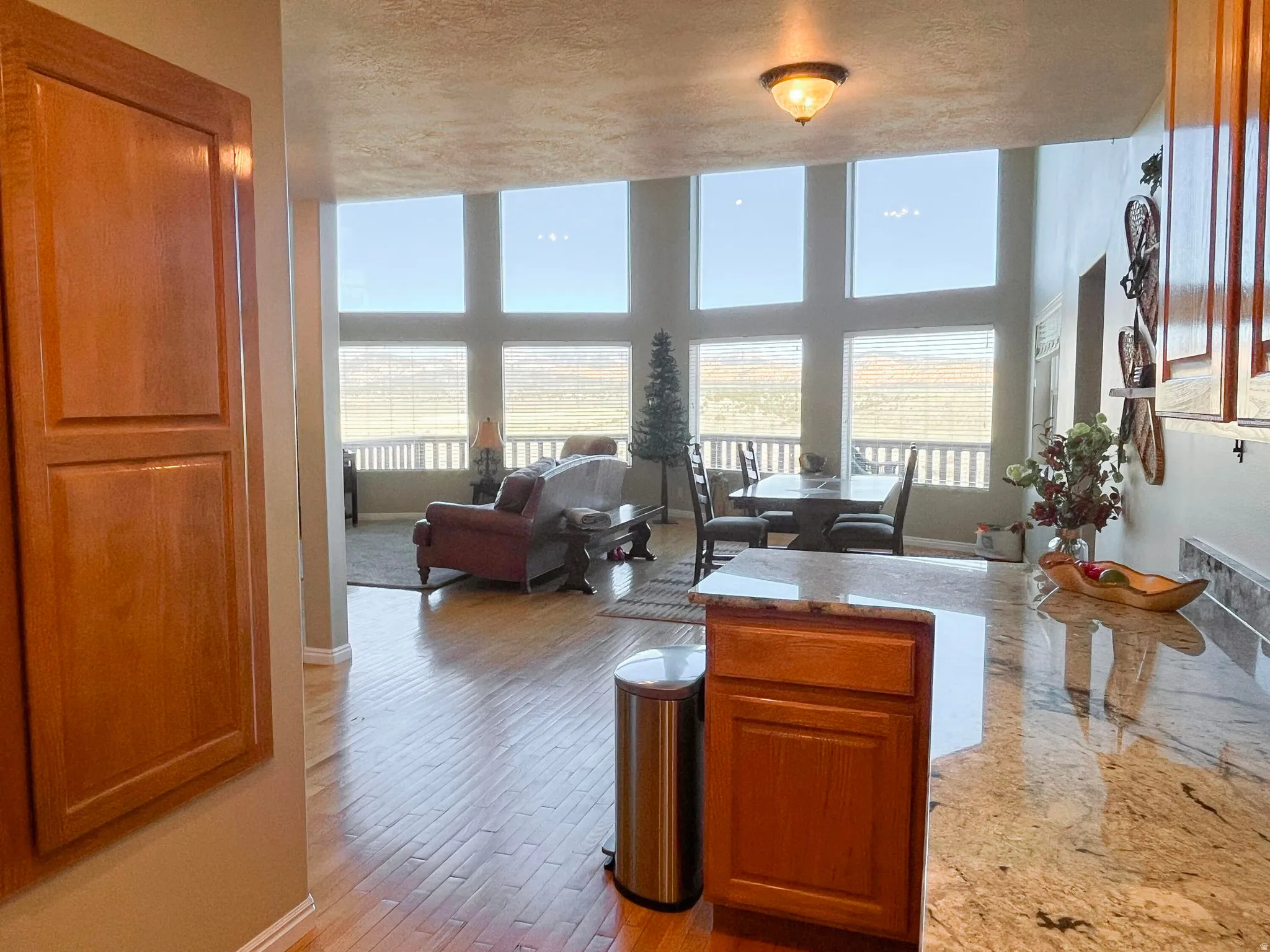 Open-concept living space with expansive windows, light wood-finish flooring, and a kitchen island featuring a polished stone countertop