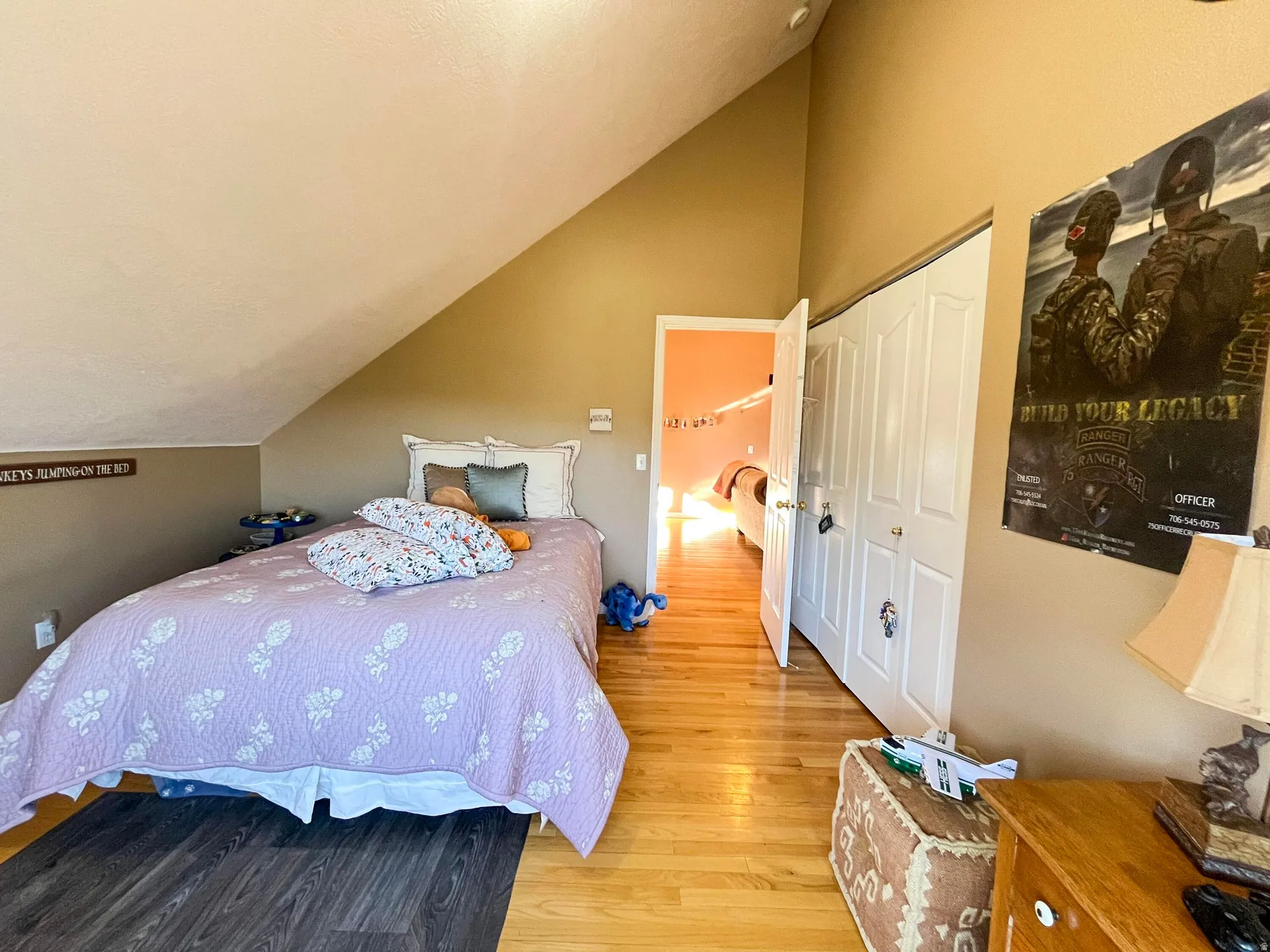 Room featuring sloped ceilings, wood-finish flooring, two-panel closet doors, and a doorway opening to an additional room