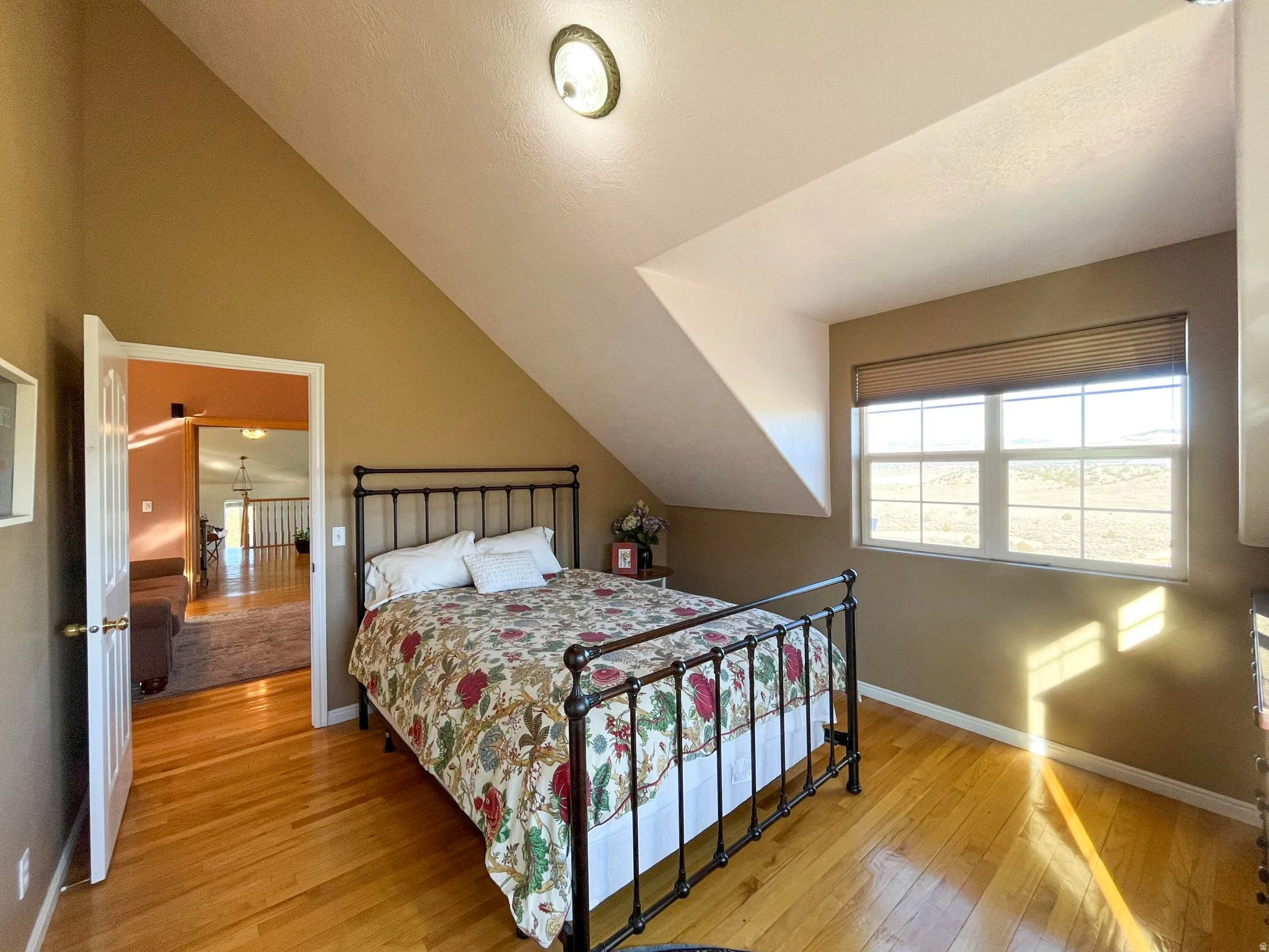 Bedroom featuring hardwood flooring, sloped ceilings, and a double-pane window with a venetian blind