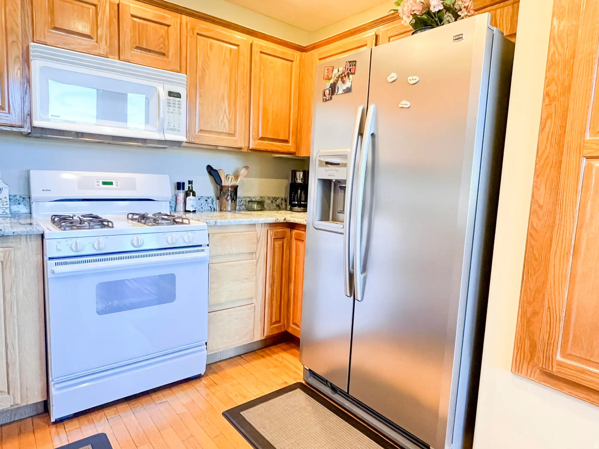 Kitchen featuring hardwood flooring, light wood cabinetry, white gas range with overhead microwave, stainless steel side-by-side refrigerator, and stone-look countertops